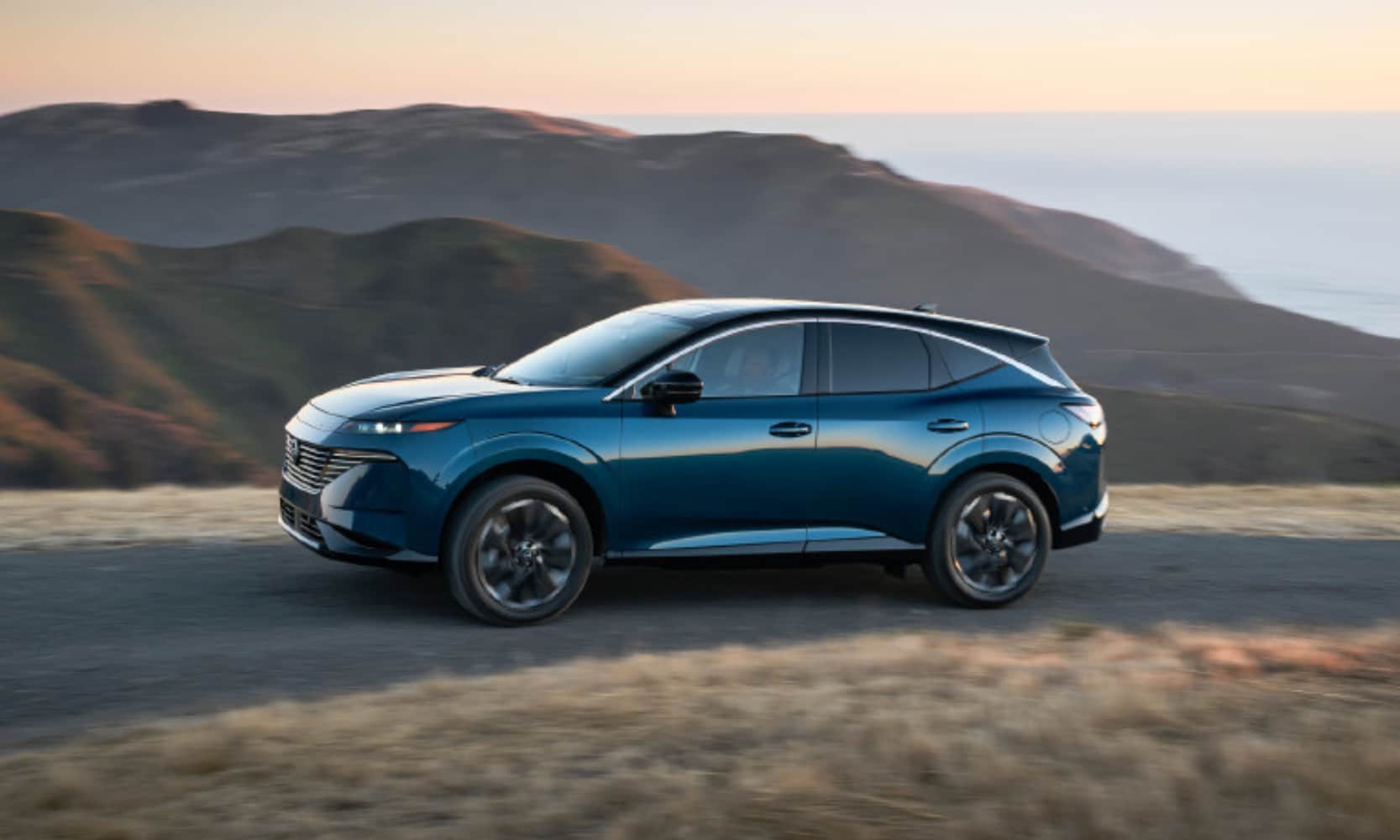Exterior side image of a blue 2025 Nissan Murano Platinum driving on a mountain