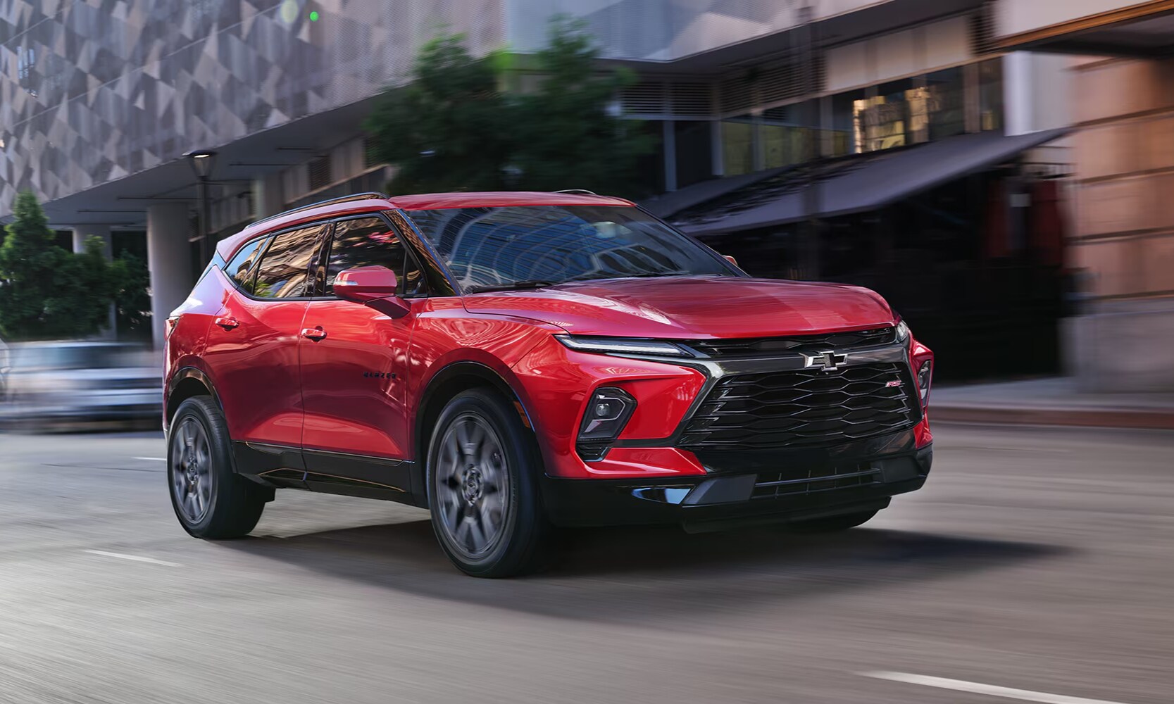 Exterior image of a red 2024 Chevy Blazer driving down a city street past buildings