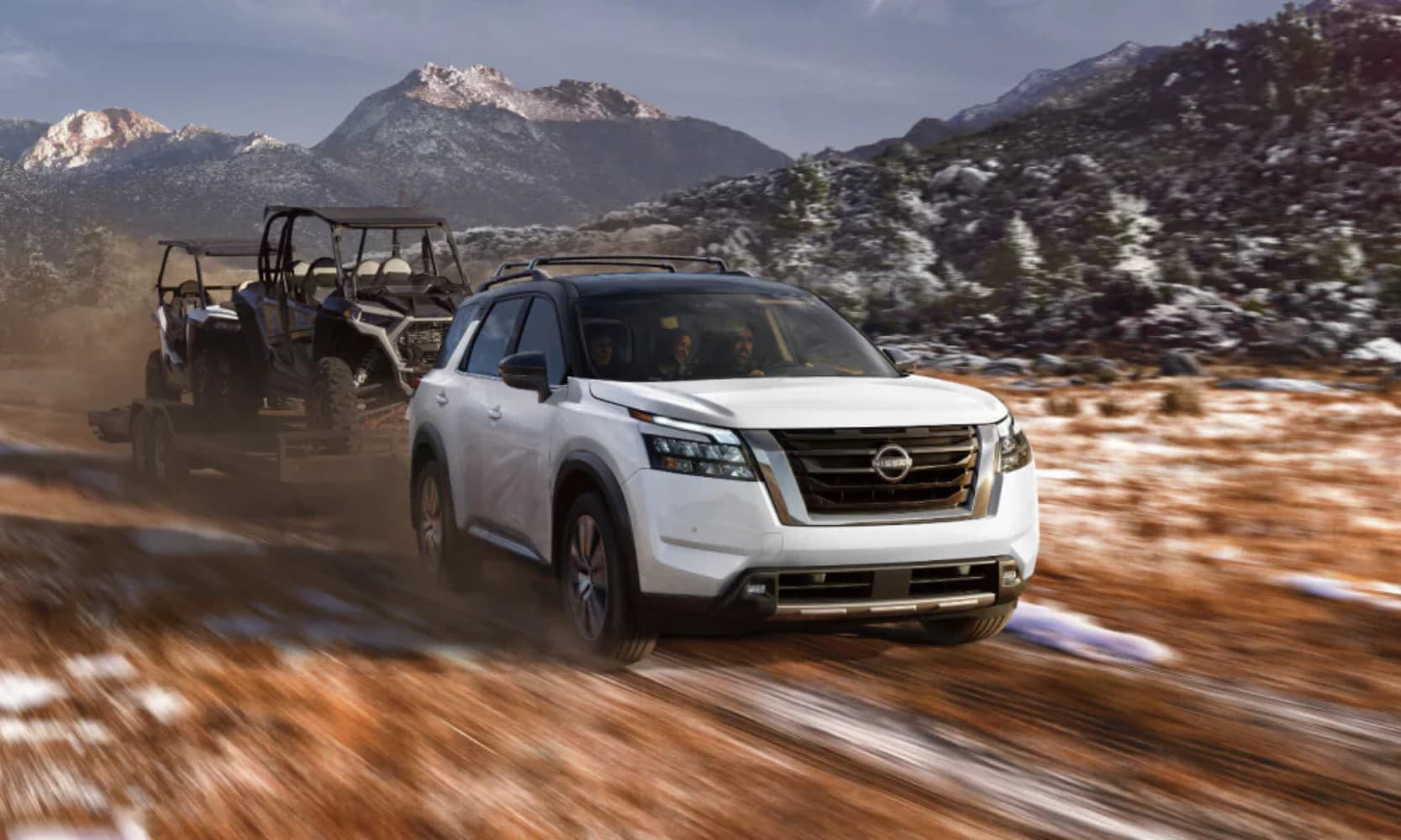 Exterior front-view image of a white 2025 Nissan Pathfinder towing an ATV in a snowy mountain landscape