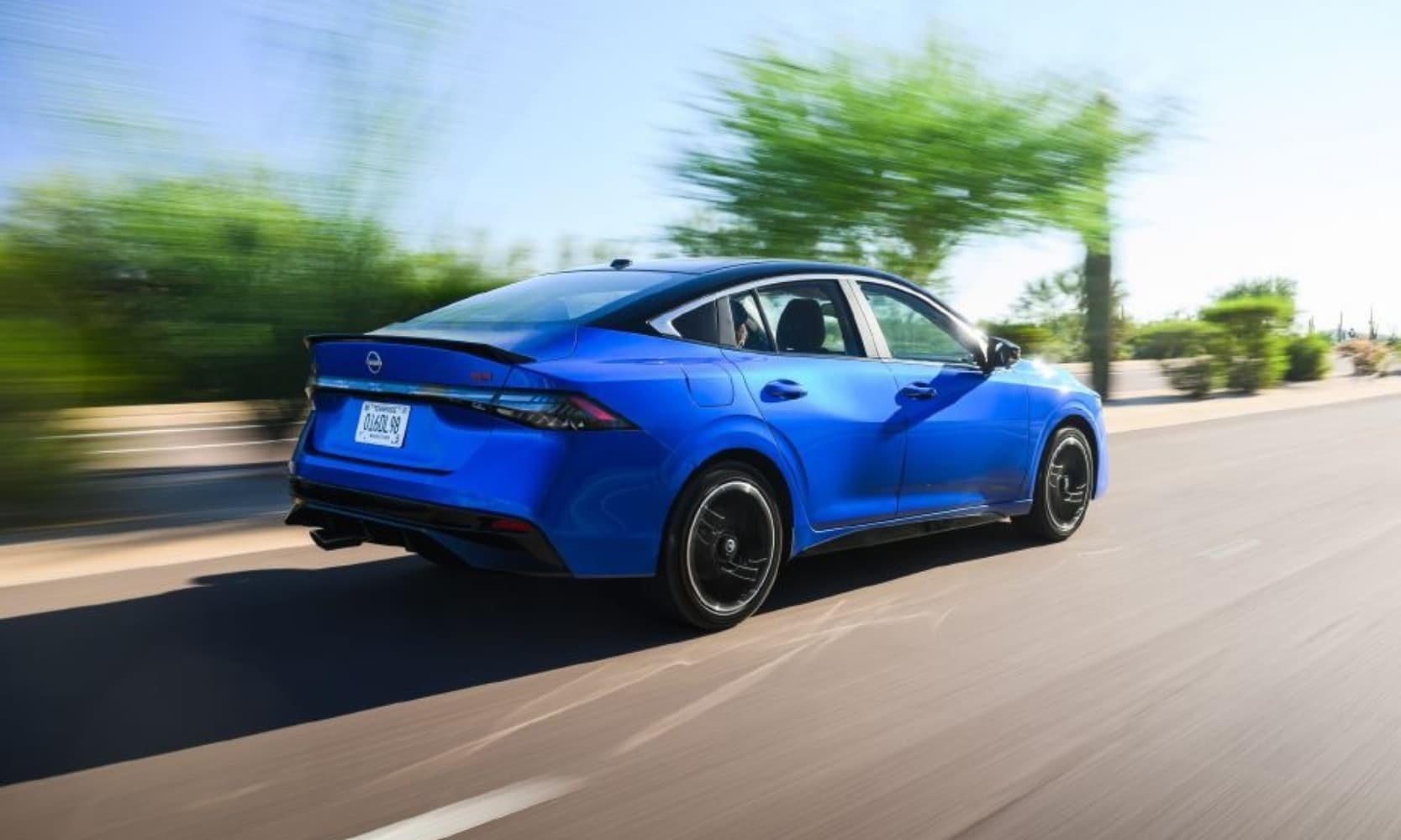 Exterior rear-view image of a blue 2027 Nissan Sentra SR driving on a tree-lined road