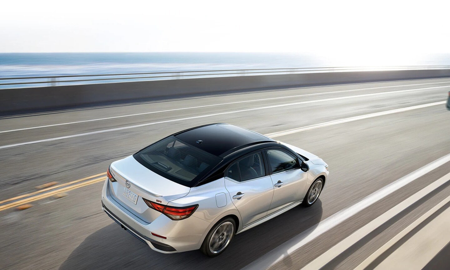 Exterior top view image of a white 2025 Nissan Sentra driving on an open waterfront freeway