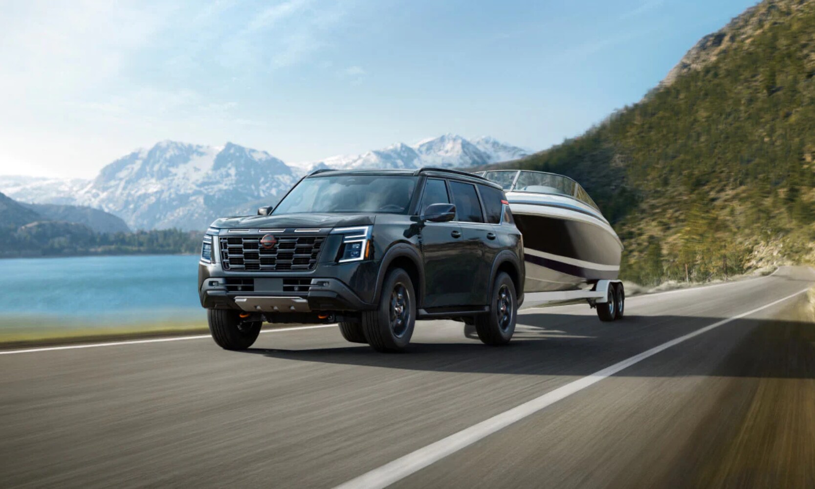 Exterior front image of a light green 2025 Nissan Armada PRO-4X towing a boat on a waterfront open highway with mountains in the background