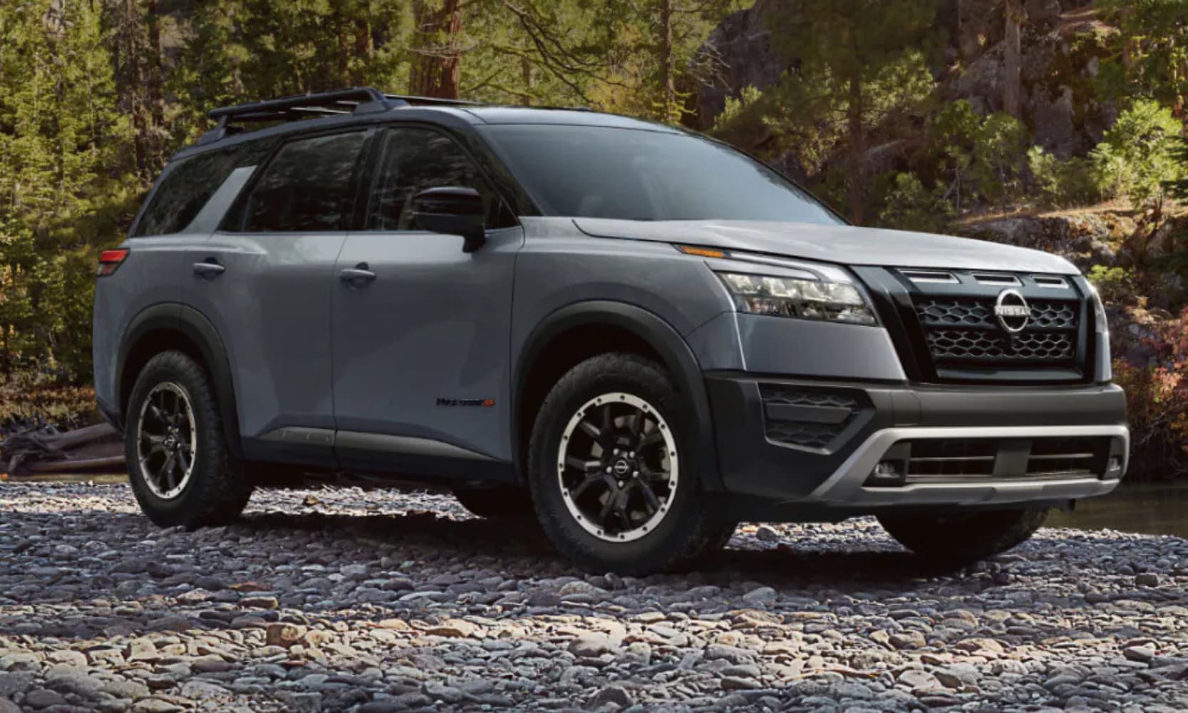 Exterior front side image of a light gray 2025 Nissan Pathfinder Rock Creek parked on a rocky road in a park landscape