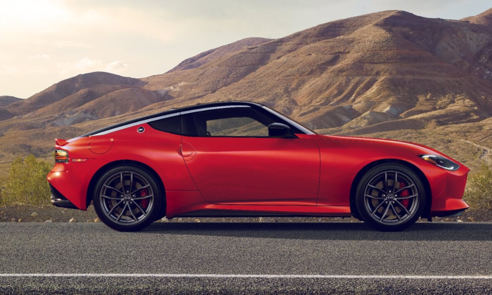 Exterior side image of a red 2025 Nissan Z Performance parked on an open freeway with mountains in the background