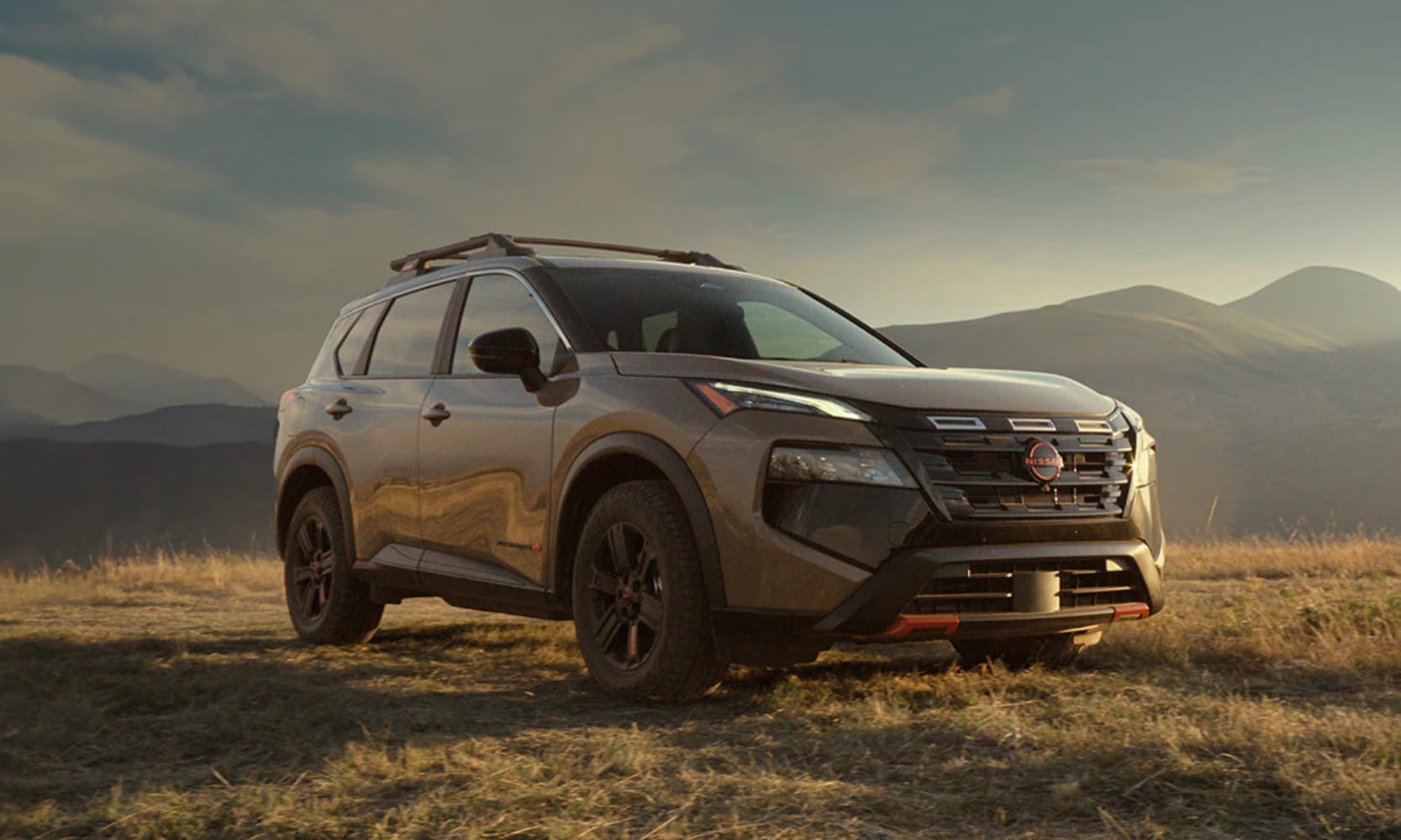 Exterior image of a light brown 2025 Nissan Rogue Rock Creek parked in a mountainous field during sunset