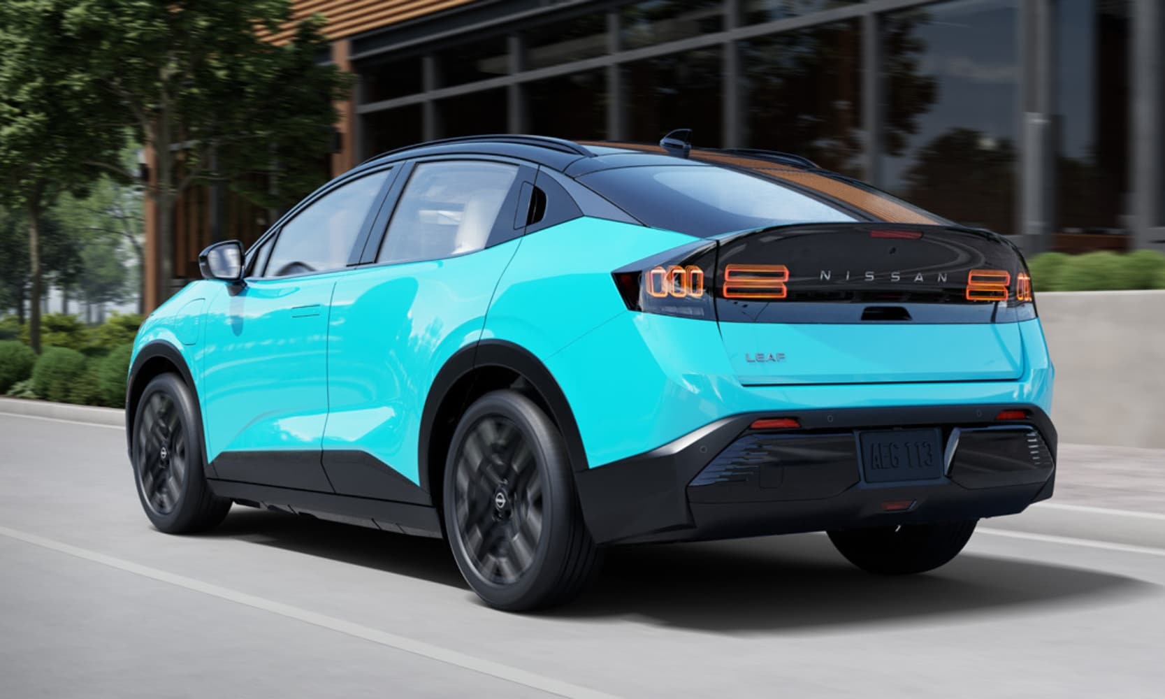 Exterior rear side angle image of an aqua blue 2026 Nissan LEAF Platinum+ driving down a road in front of a building