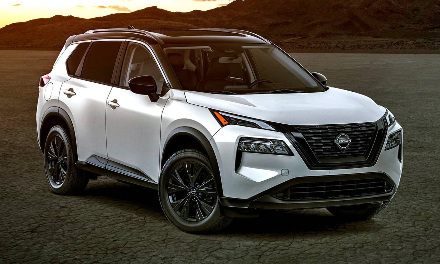 Exterior side angle image of a white 2024 Nissan Rogue SV parked in a mountainous setting during sunset