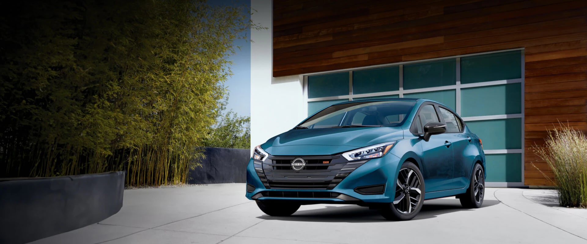 Exterior front hero image of a teal 2025 Nissan Versa parked in a home’s driveway