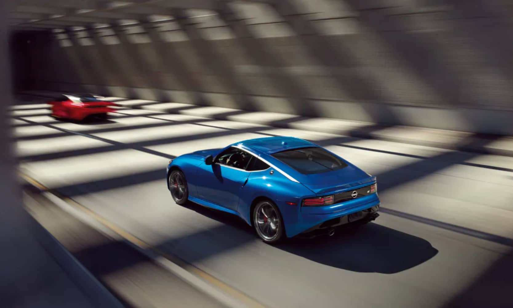 Top rear view angle image of a blue 2025 Nissan Z driving in an enclosed freeway behind a red car