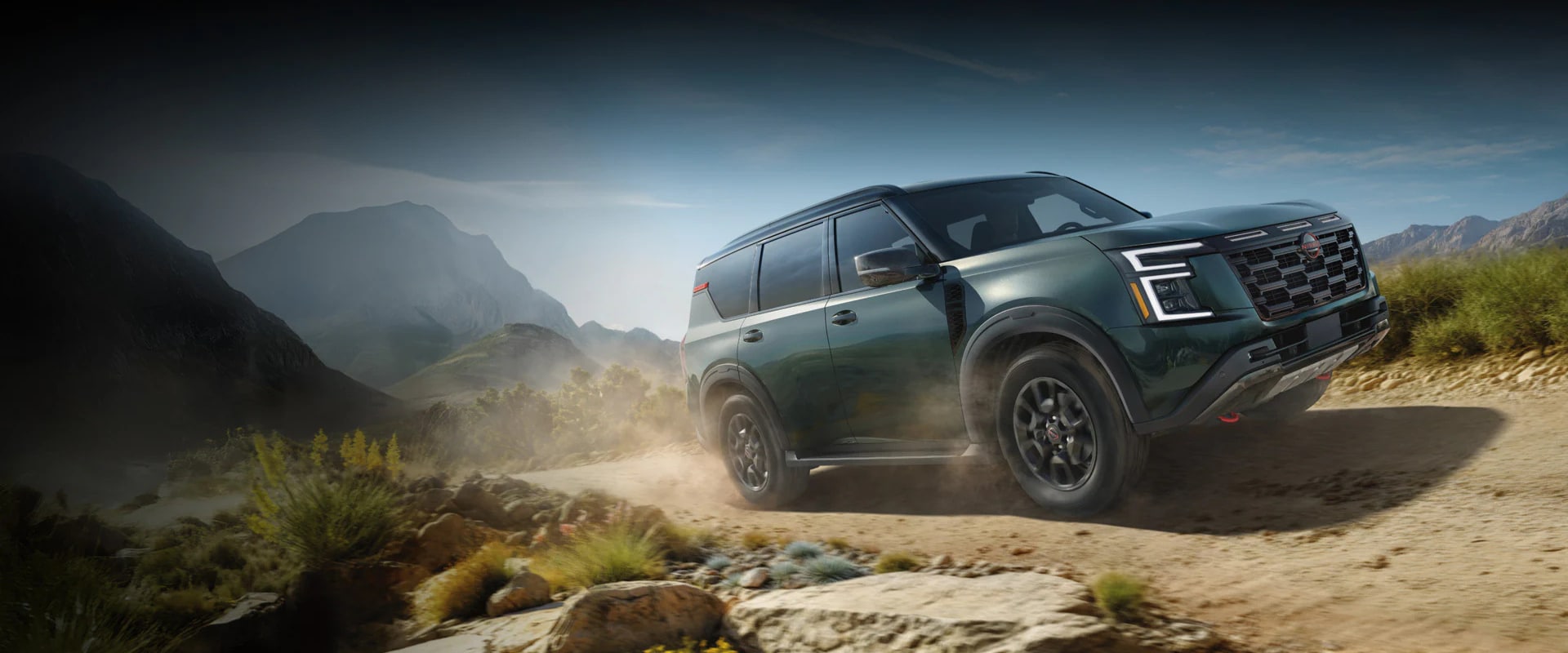 Exterior image of a light green 2025 Nissan Armada driving up a dirt hill in a mountainous setting
