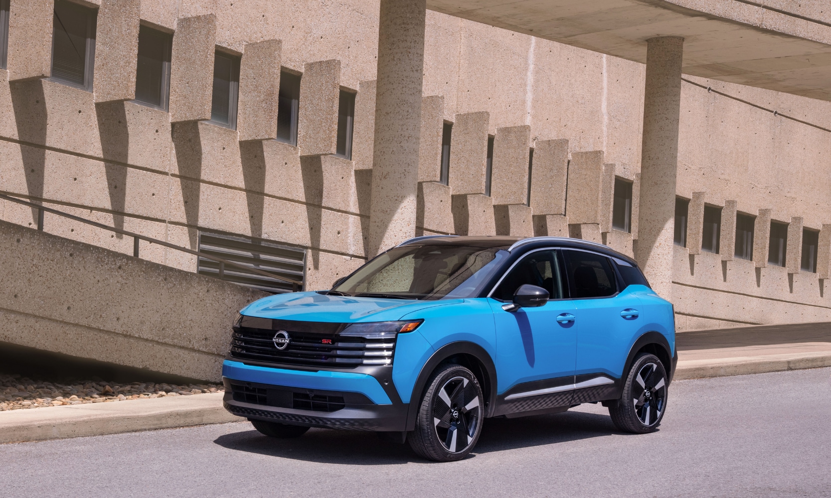 Image of a light blue 2024 Nissan Kicks driving on an overpass highway