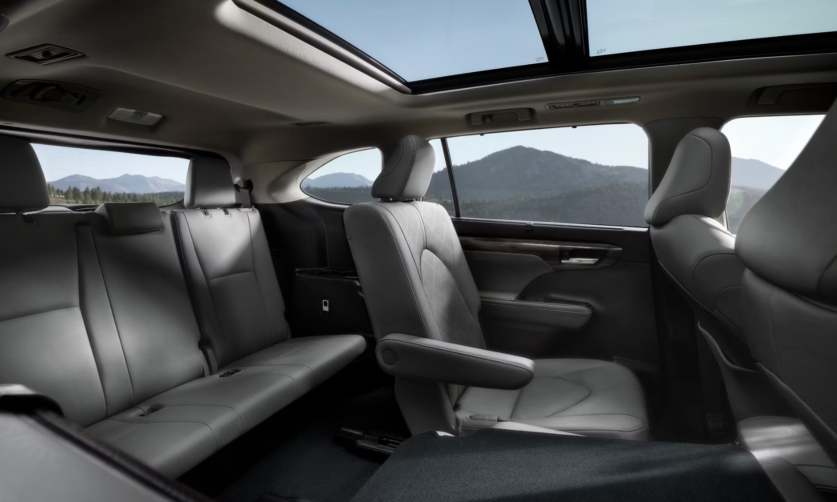 Interior image of the 2025 Toyota Highlander's three-row leather gray seats with the sunroof showing mountain views
