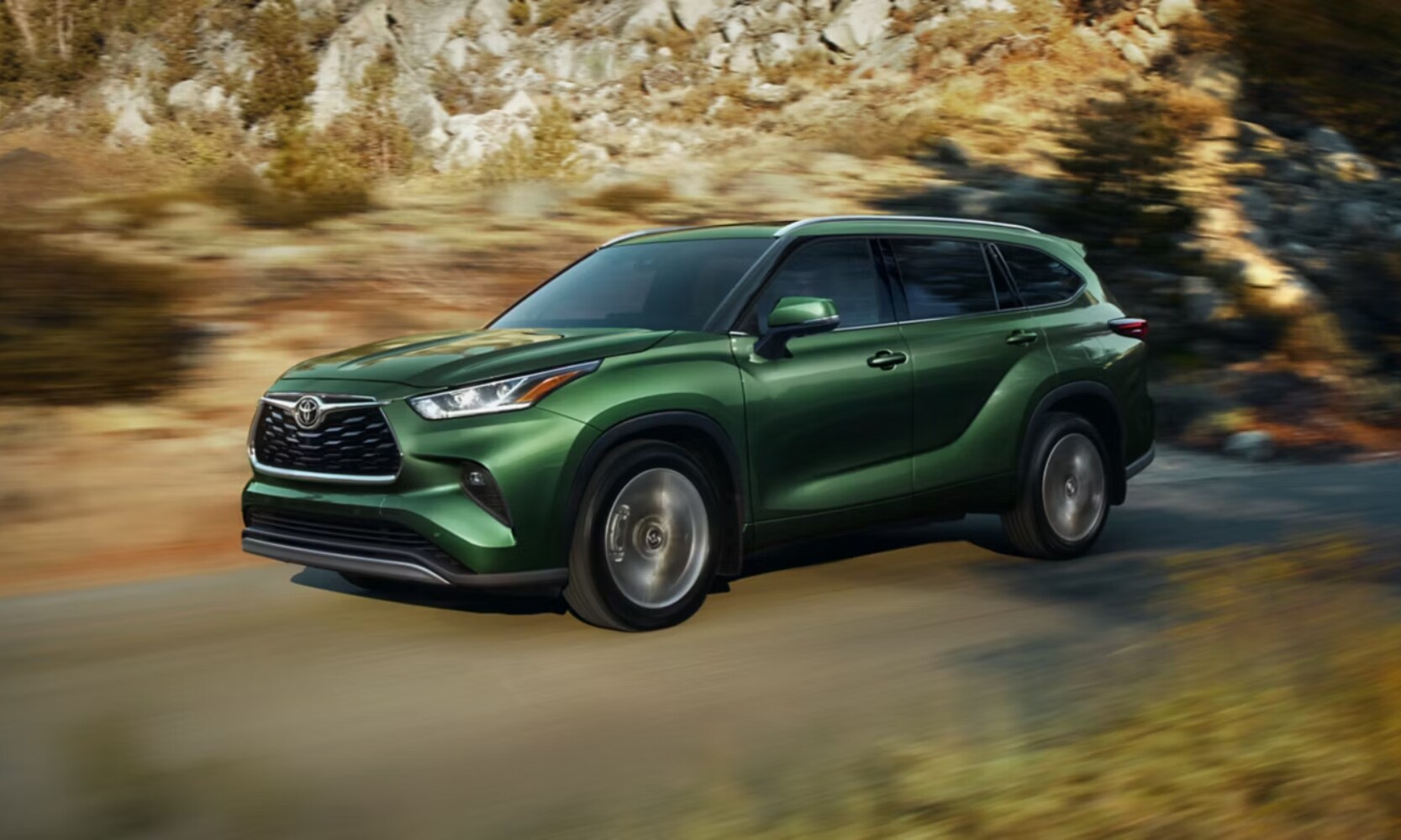 Exterior side image of a green 2025 Toyota Highlander Platinum driving through a mountain road