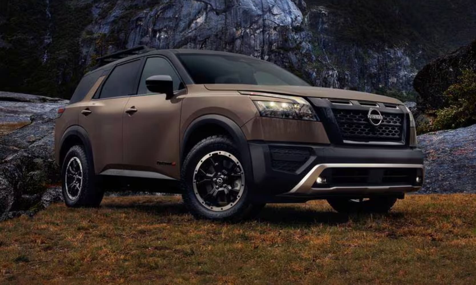 Closeup exterior angle image of a tan 2023 Nissan Pathfinder Rock Creek parked in front of a rocky mountain