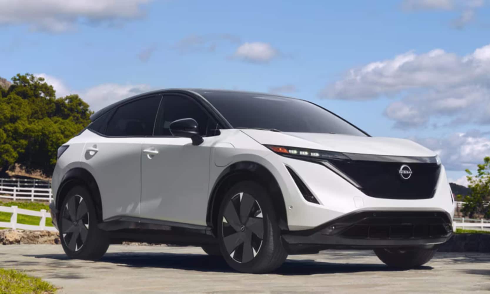 2026%20Nissan%20ARIYA%20Trims%20%20Nissan%20of%20Silsbee%20TX.png Exterior image of a white 2026 Nissan ARIYA parked in a rural home driveway