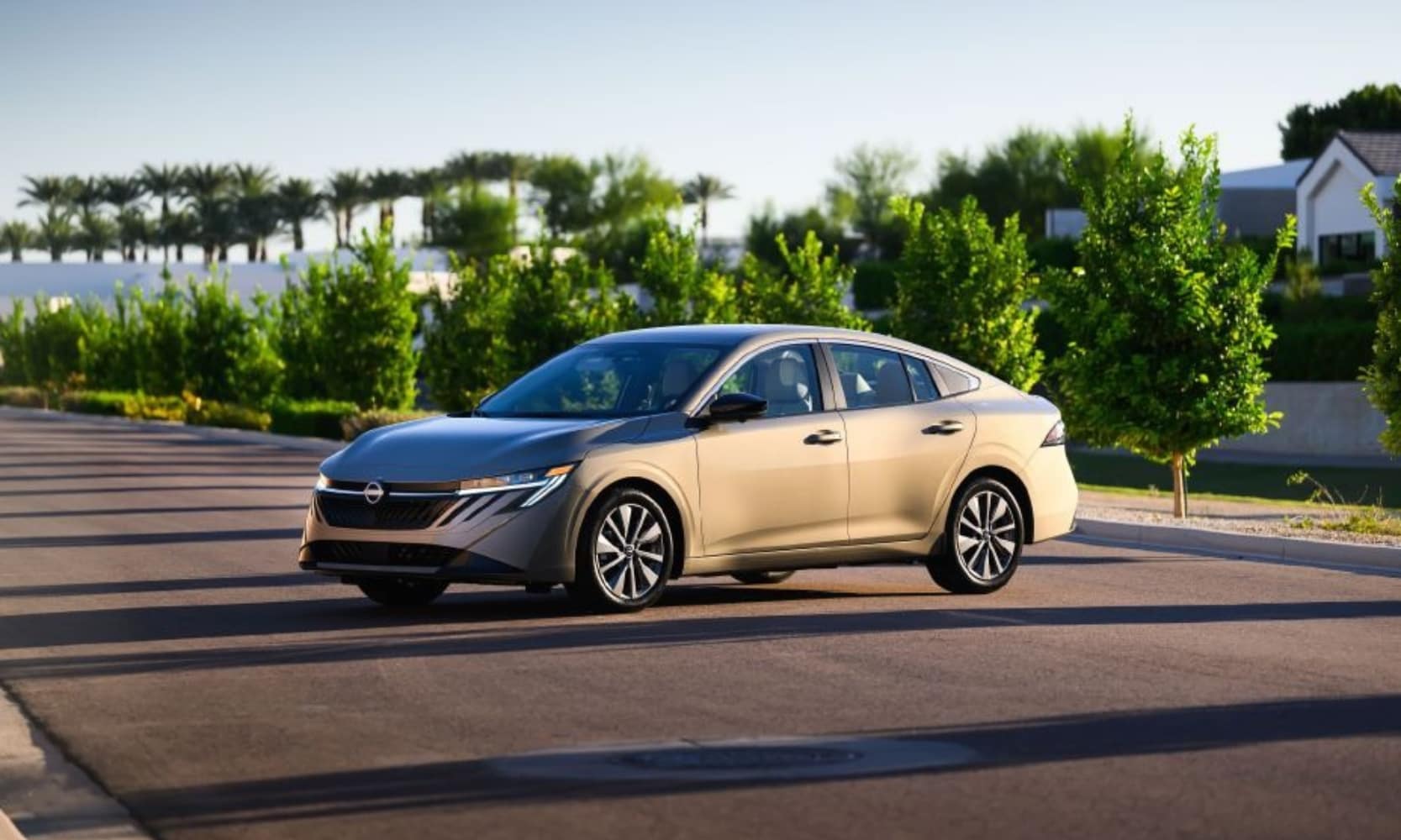 Exterior side image of a tan 2027 Nissan Sentra SL parked on a tree-lined suburban street in a tropical area