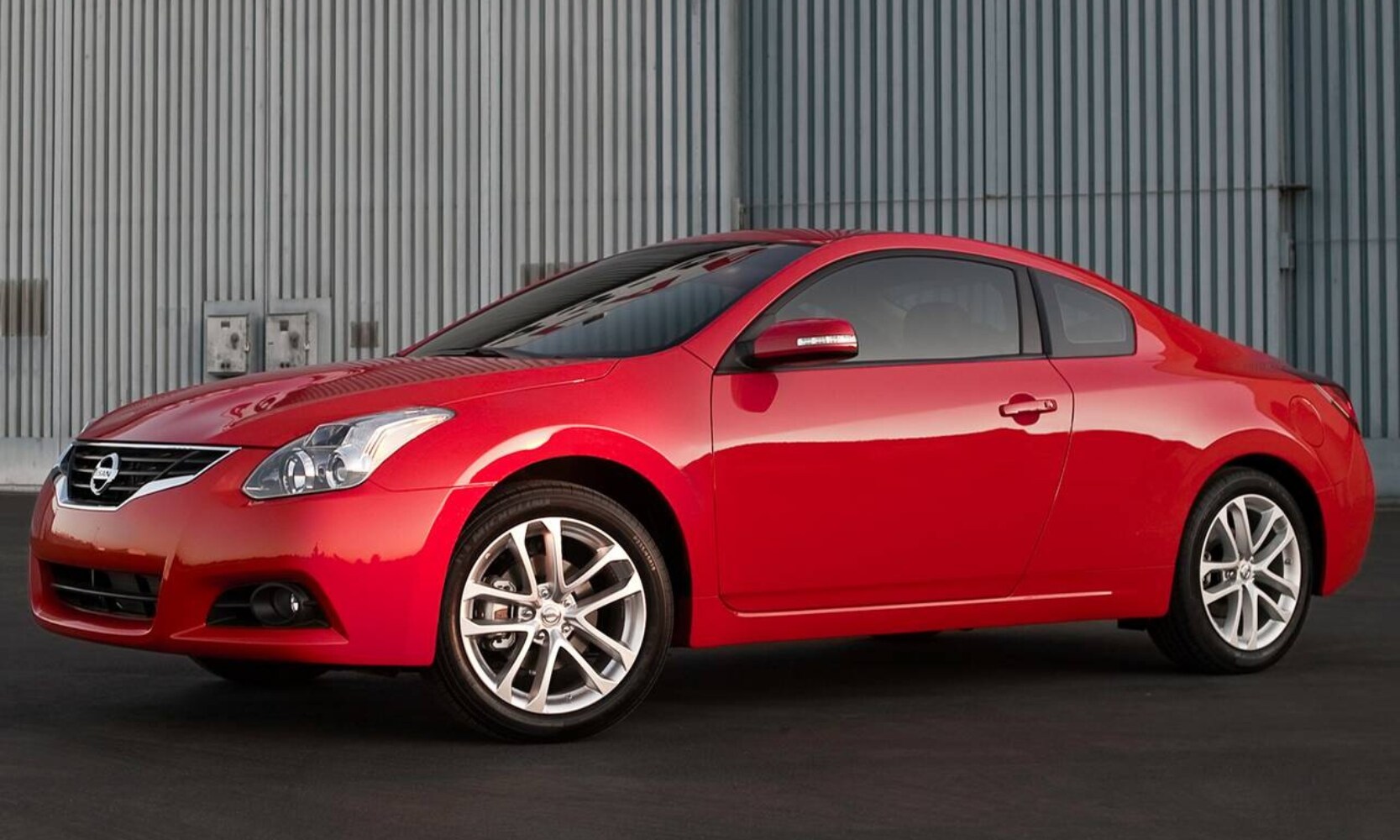 Exterior front side view image of a red 2010 Nissan Coupe parked outside a building