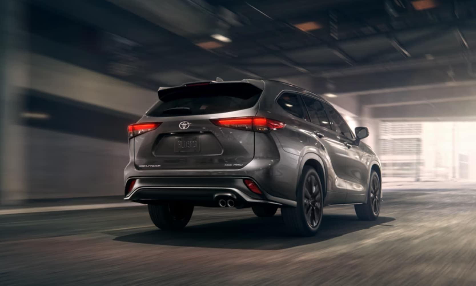Exterior rear-view image of a dark gray 2025 Toyota Highlander driving through an enclosed city freeway