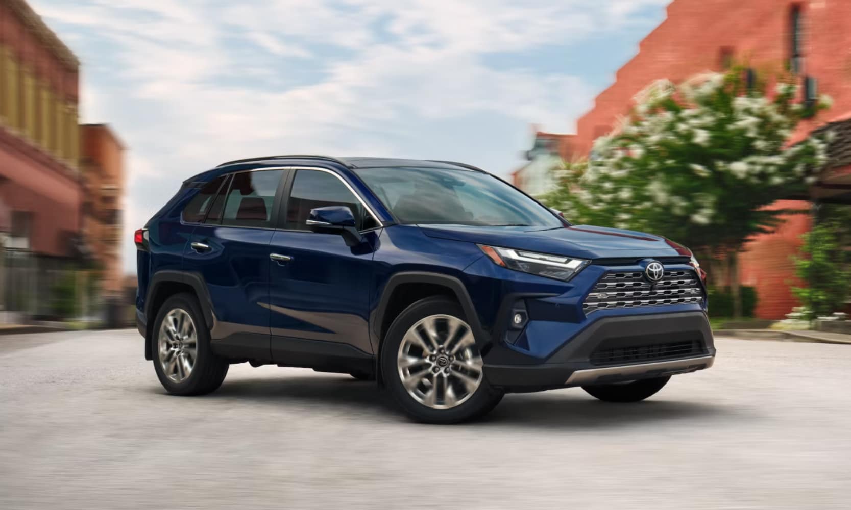 Exterior image of a blue 2025 Toyota RAV4 Limited trim parked outside a downtown area during the day