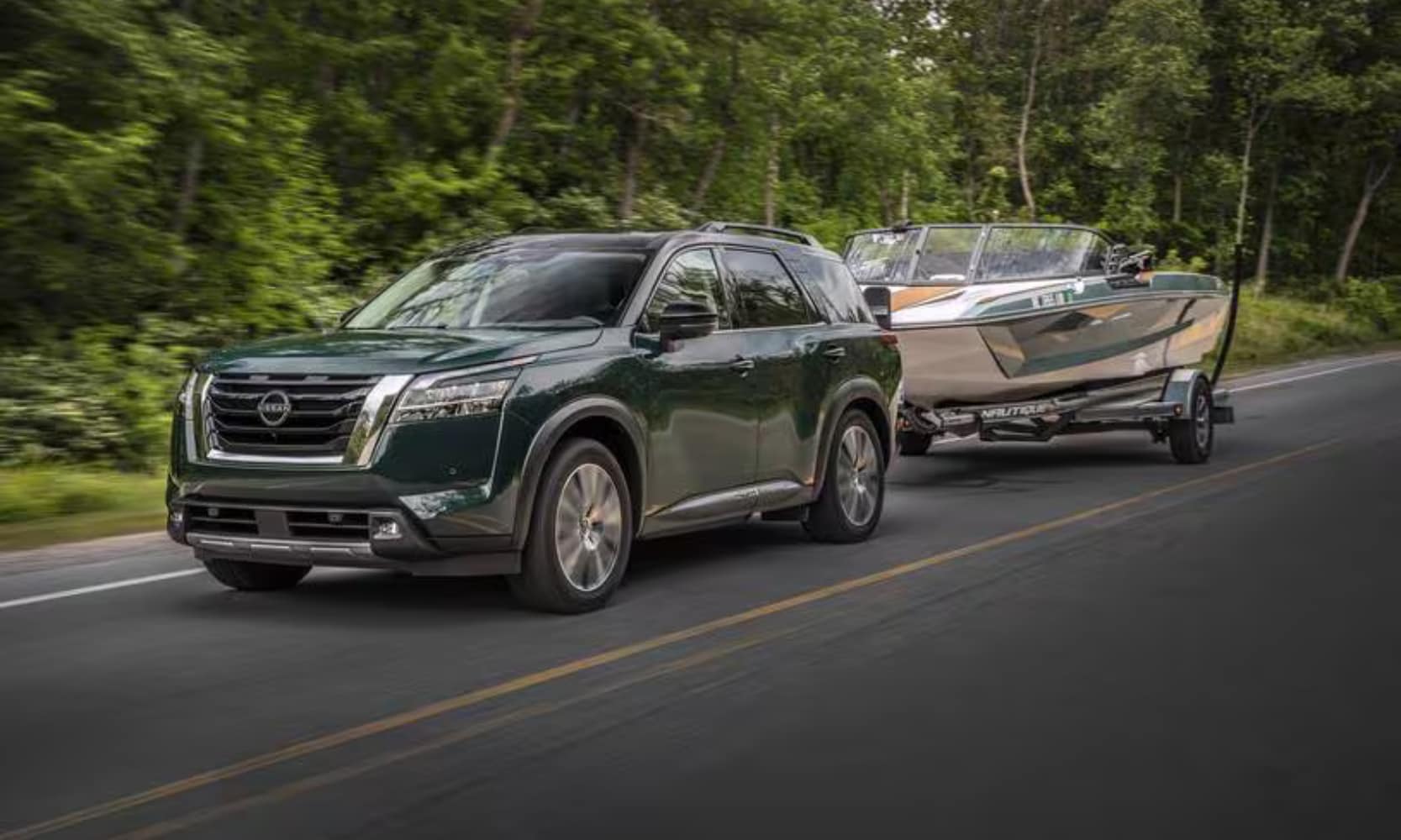 Image of a green 2025 Nissan Pathfinder towing a small boat on a tree-lined road