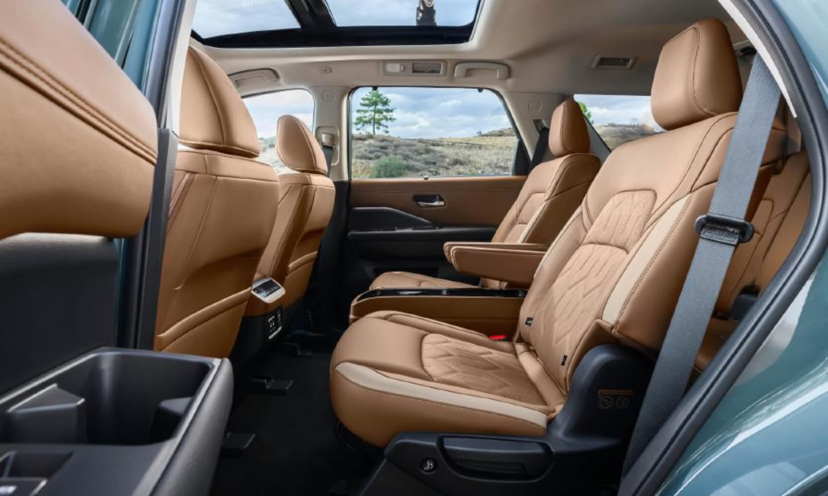 Interior image of a 2026 Nissan Pathfinder first and second row tan leather seats with a sunroof and hills in the windows