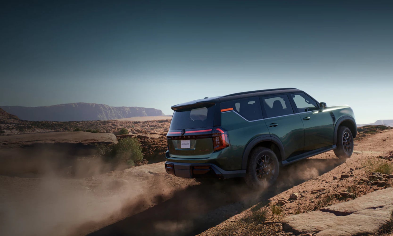 Exterior rear side image of a green 2025 Nissan Armada PRO-4X off-roading up a rocky hill with dirt blowing behind the wheel