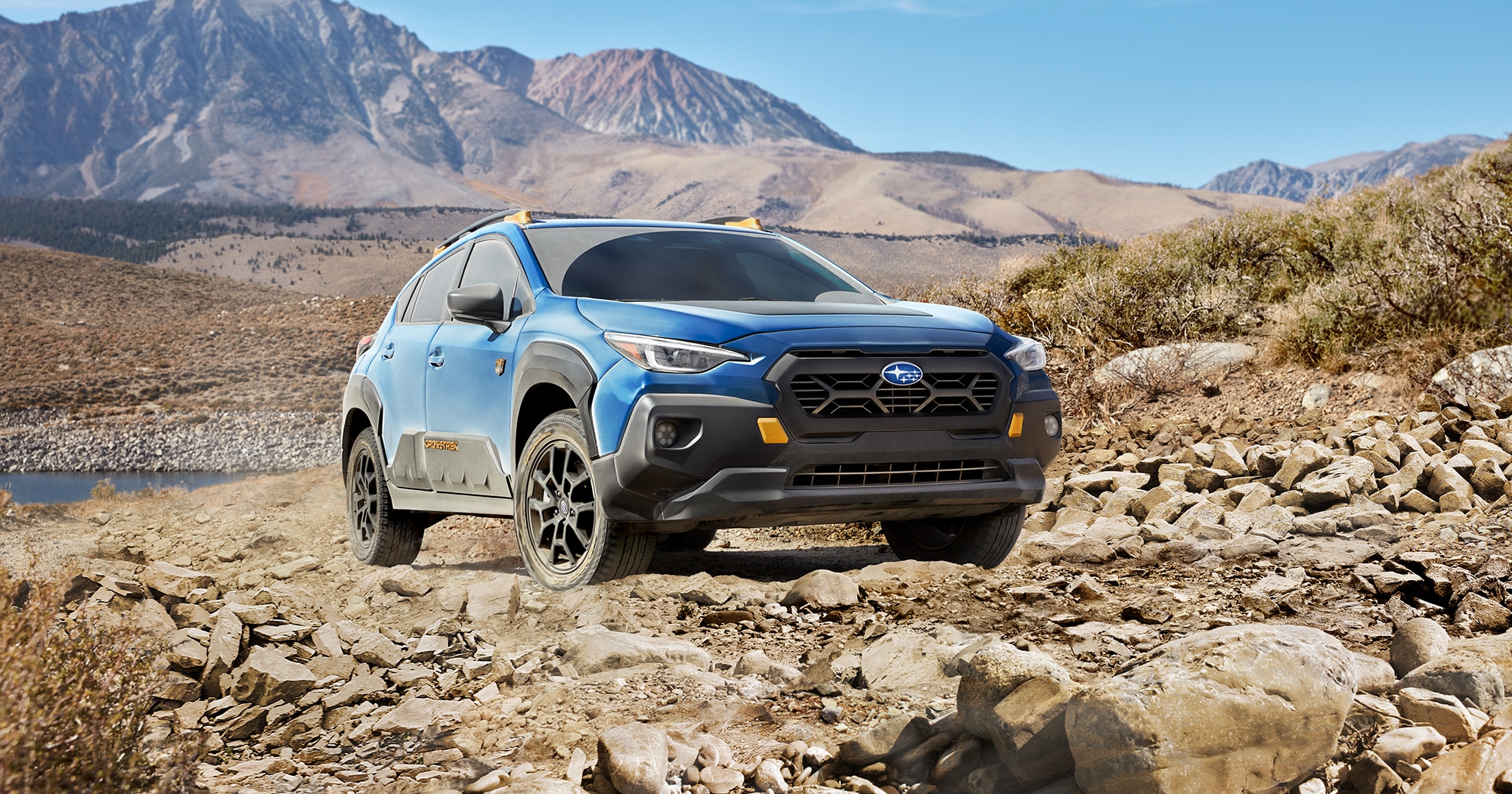  A blue off road Subaru Crosstrek Wilderness SUV parked on rocky terrain with mountains in background