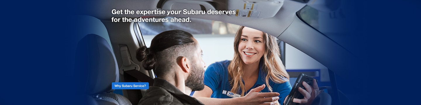 Person sitting in a Subaru having a discussion with a service technician standing outside the vehicle.