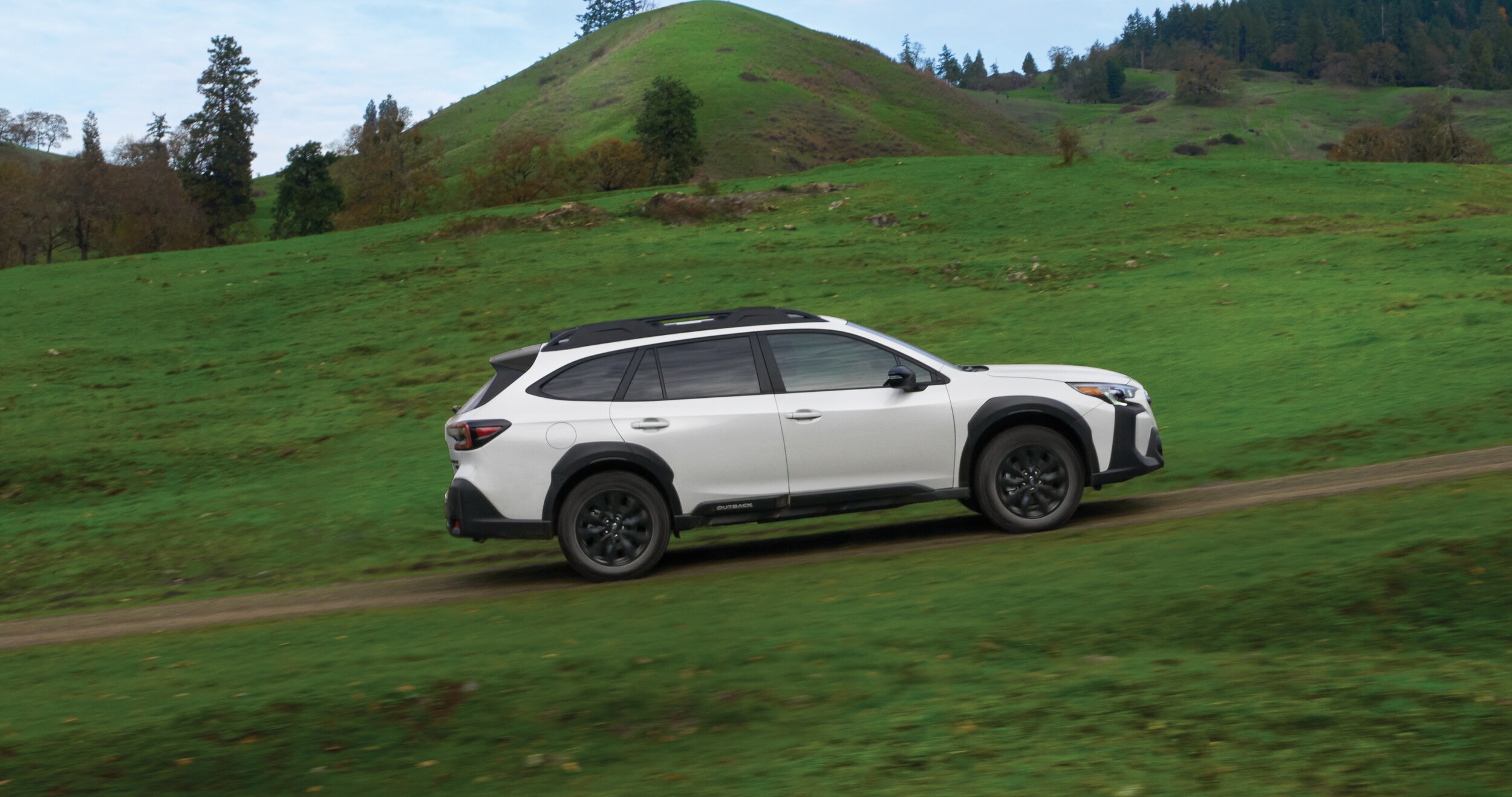 A couple getting ready for a hike near their 2023 Outback Onyx Edition, which is towing a camping trailer.