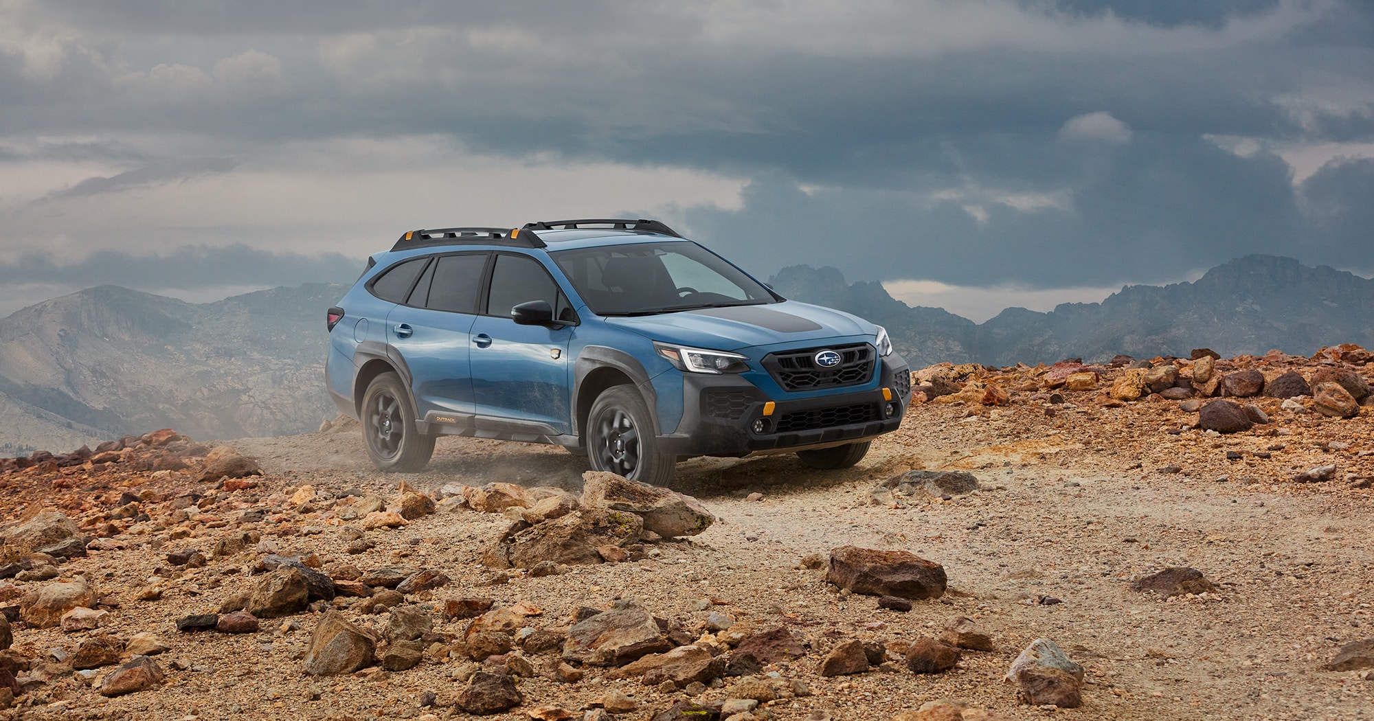 A blue Subaru Outback Wilderness off road SUV parked on a cliff overlooking mountains.