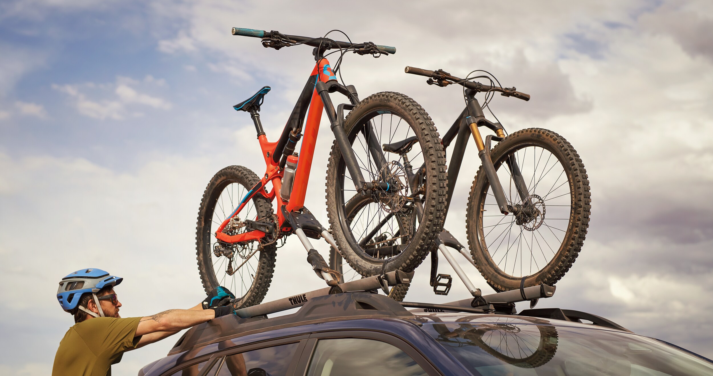 A man mounting bikes onto an available bike carrier on the raised roof rails of the 2023 Outback.