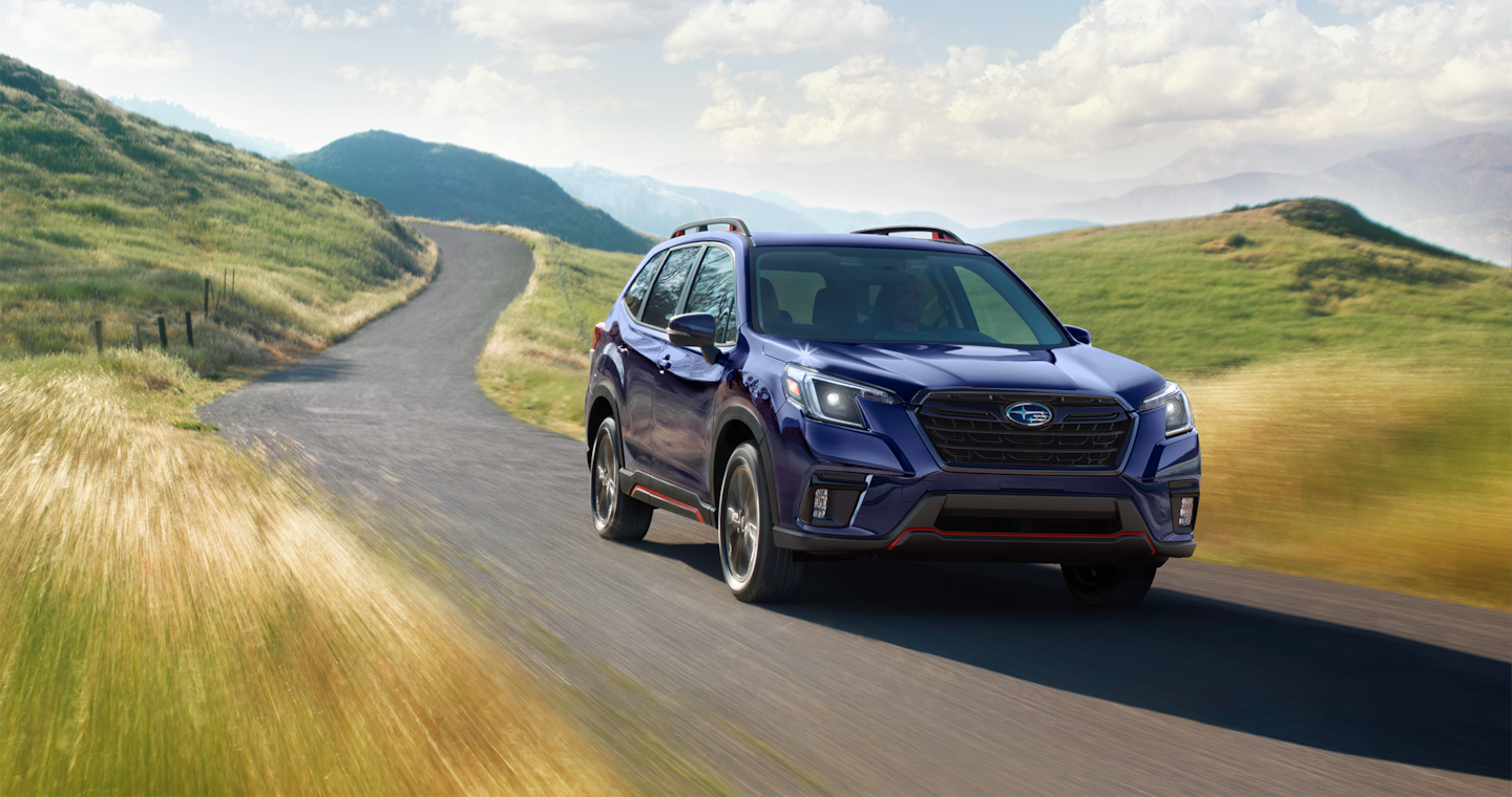 A blue 2024 Subaru Forester 5-seater SUV drives through the countryside