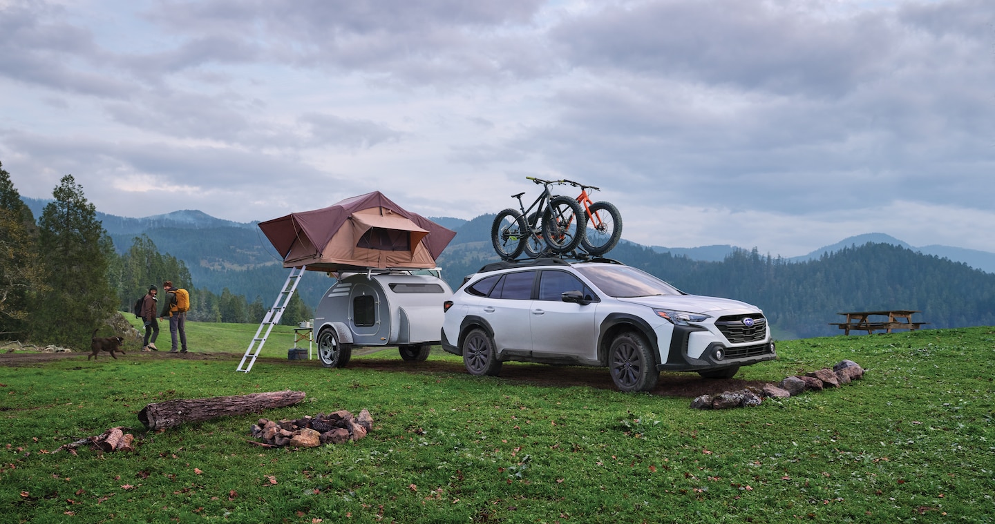 A Subaru Outback attached to a camper with a roof tent and 2 bicycles on its roof