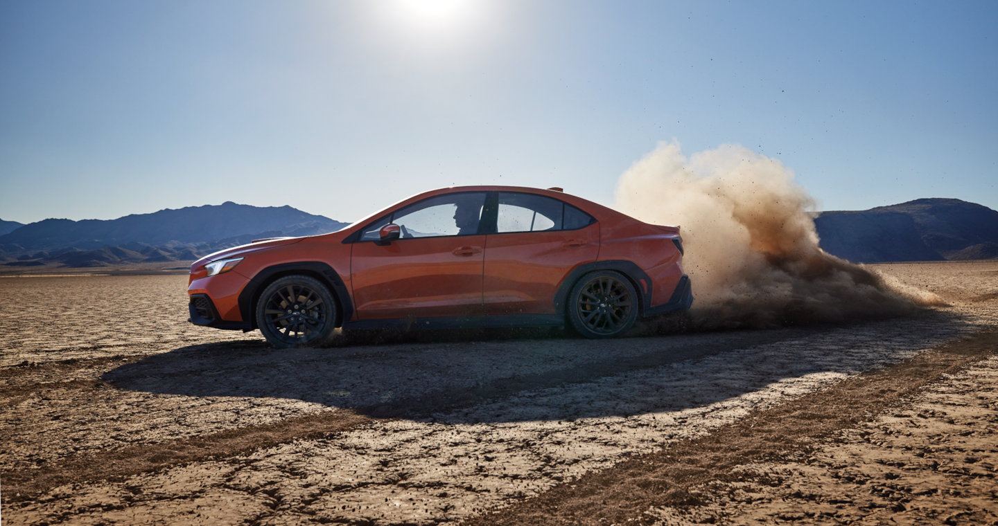  A 2024 Subaru WRX all wheel drive sports car kicks up dust drifting a turn on a dry desert bed. 