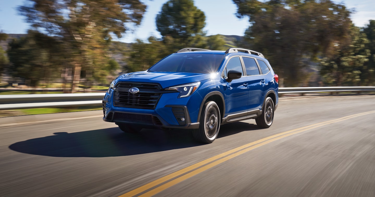 A blue Ascent 3-row SUV drives on a rural highway.