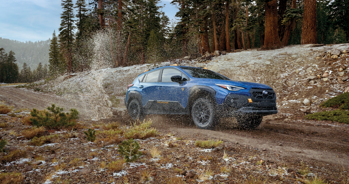 A Crosstrek Wilderness all-wheel drive SUV splashes through a puddle on a dirt road.
