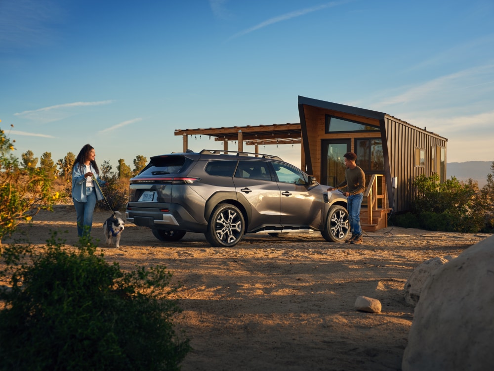 A static image of a grey 2027 Subaru Trailseeker parked on a grassy clearing in a rocky mountain landscape