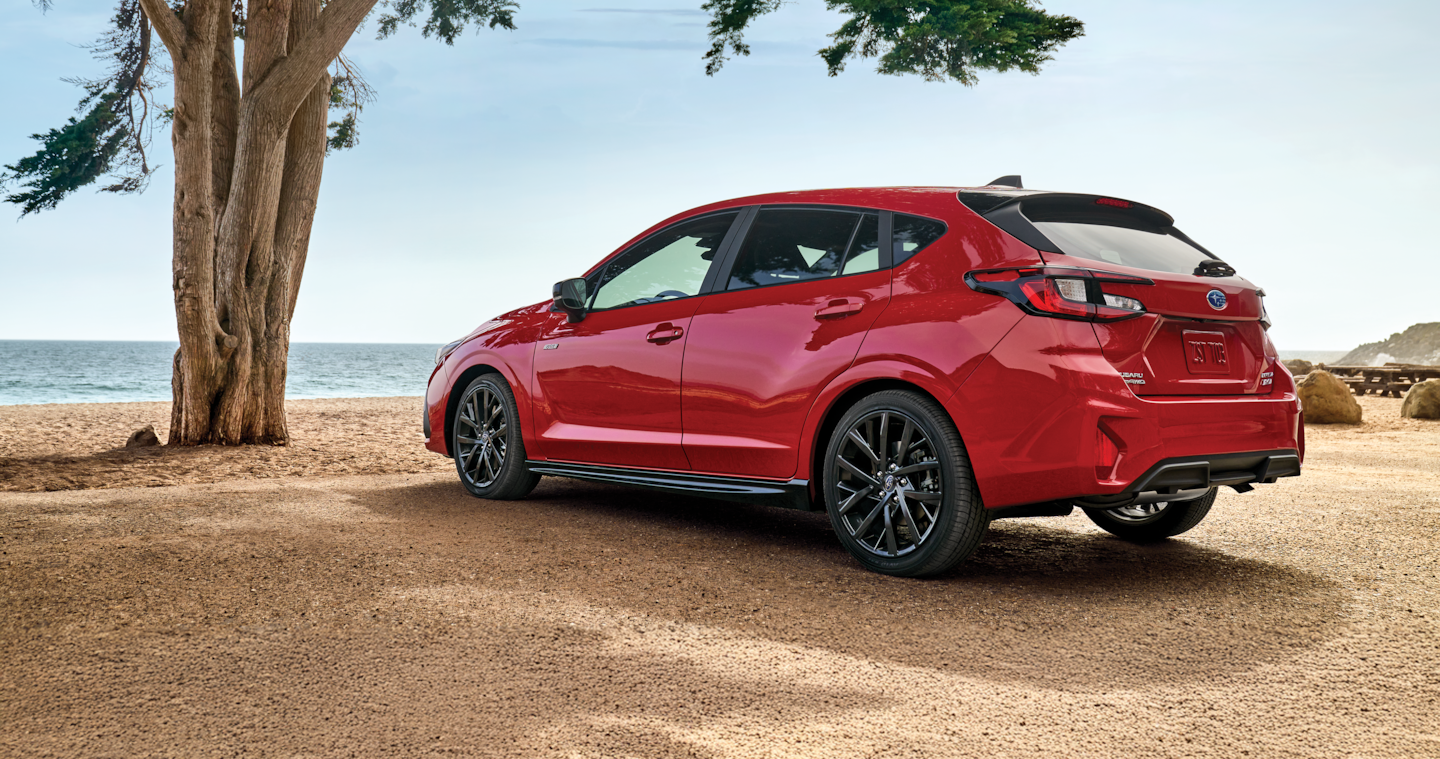 A red Impreza AWD hatchback parked by the ocean.