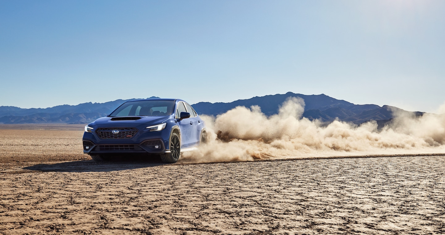  A WRX high-performance sports sedan drifts a turn on a desert bed, kicking up a cloud of dust.