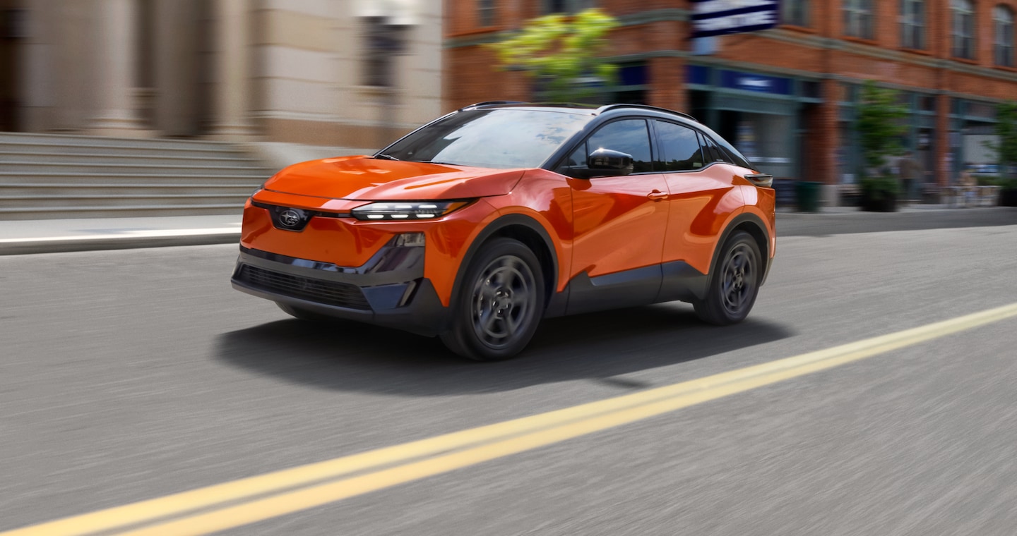 An orange Subaru Uncharted EV drives down a city street.