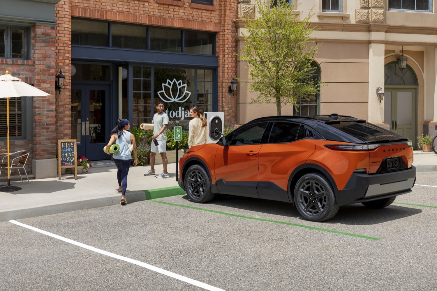  A static image of an orange 2026 Subaru Uncharted parked at an EV charging station along a city street. 