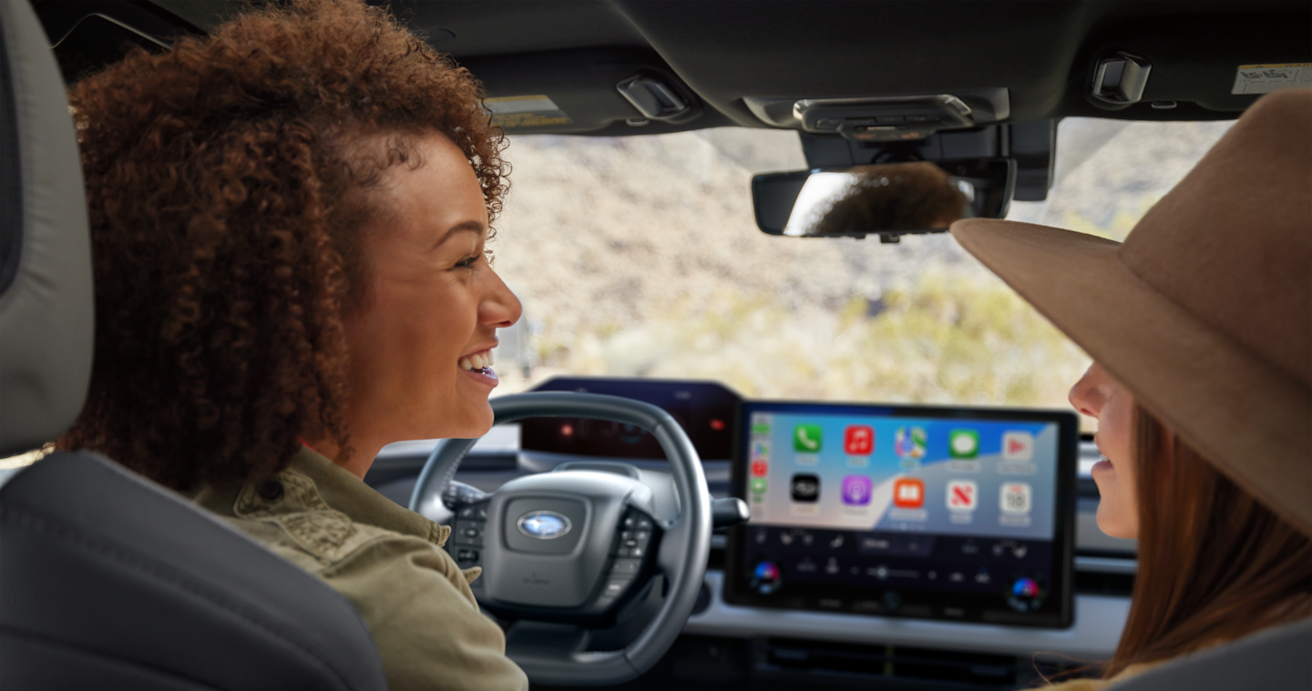  Two women talk in the front seats of a Subaru vehicle.
