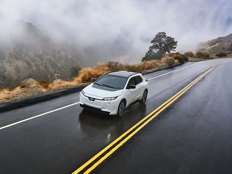 A Solterra AWD electric SUV drives on a narrow mountain road in the rain.