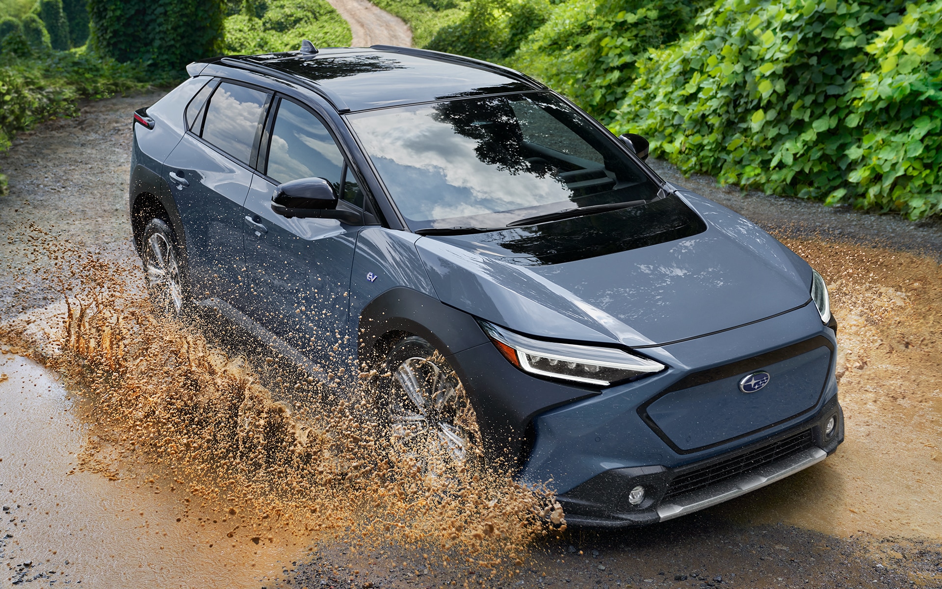 A Subaru Solterra electric family SUV drives through a large puddle on a dirt road.