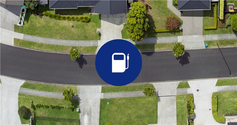  A white gas pump icon on a blue circle, superimposed on an aerial view of a road through a forest.