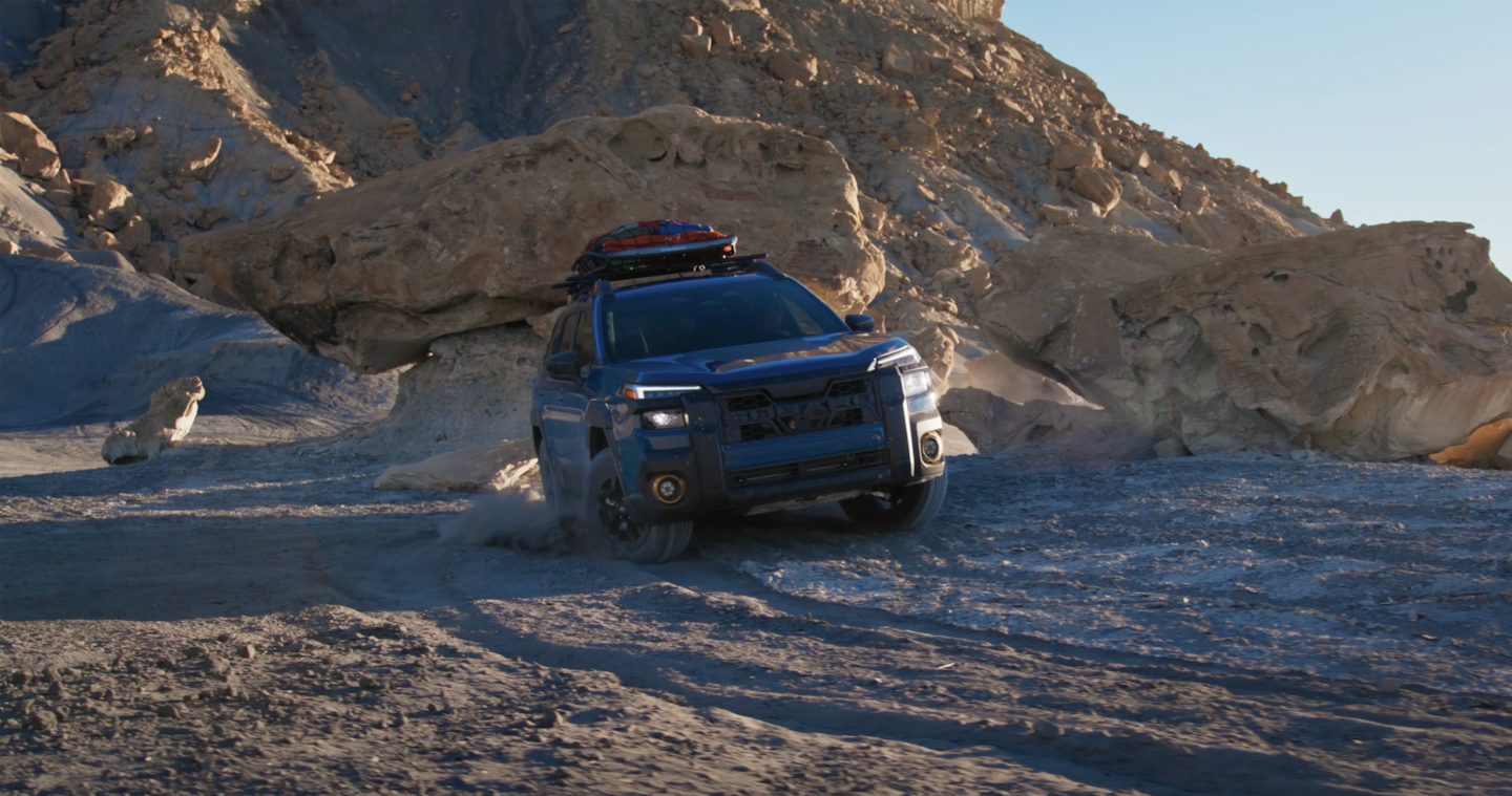  A geyser blue 2026 Subaru Outback Wilderness AWD SUV driving through various features of a desert biome.