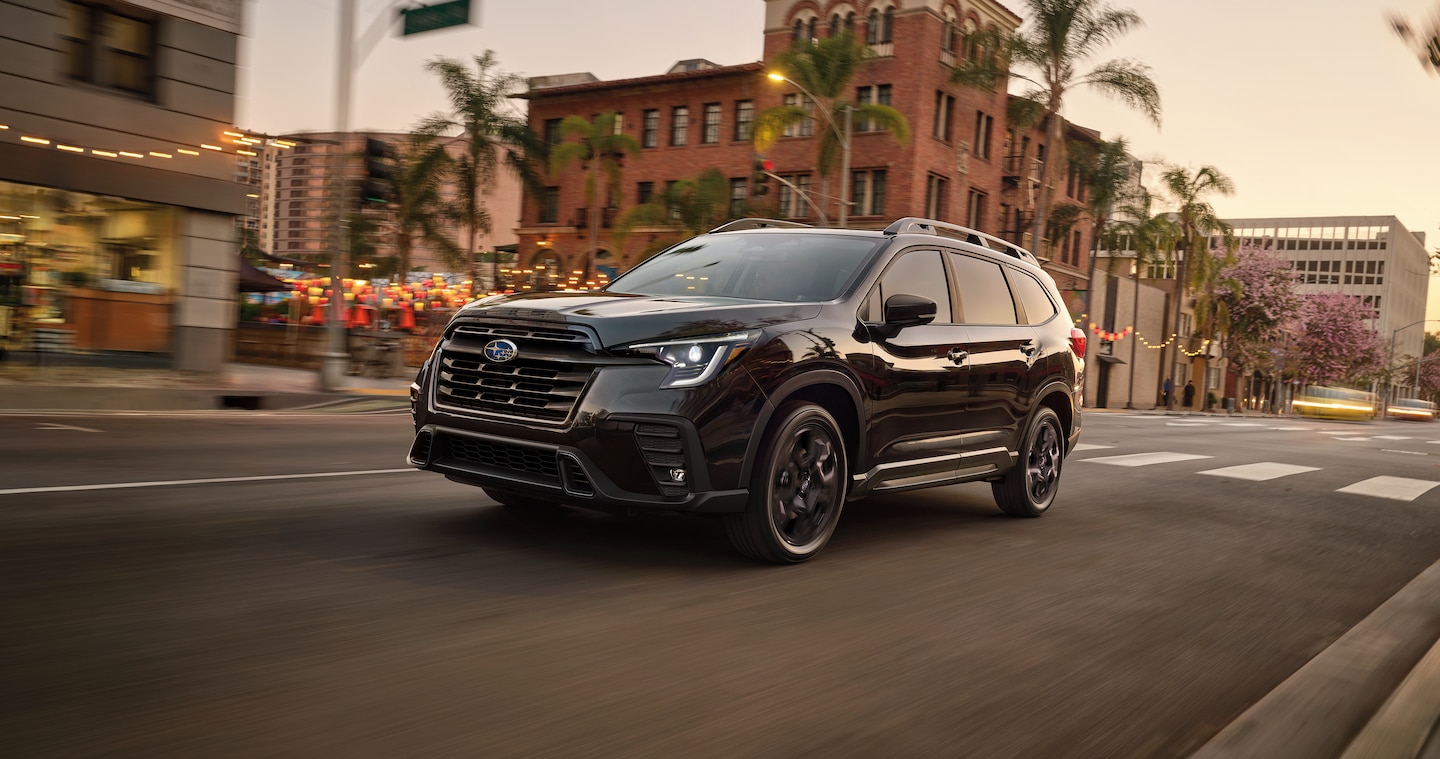 A black Subaru Ascent 3-row SUV drives on a city street.
