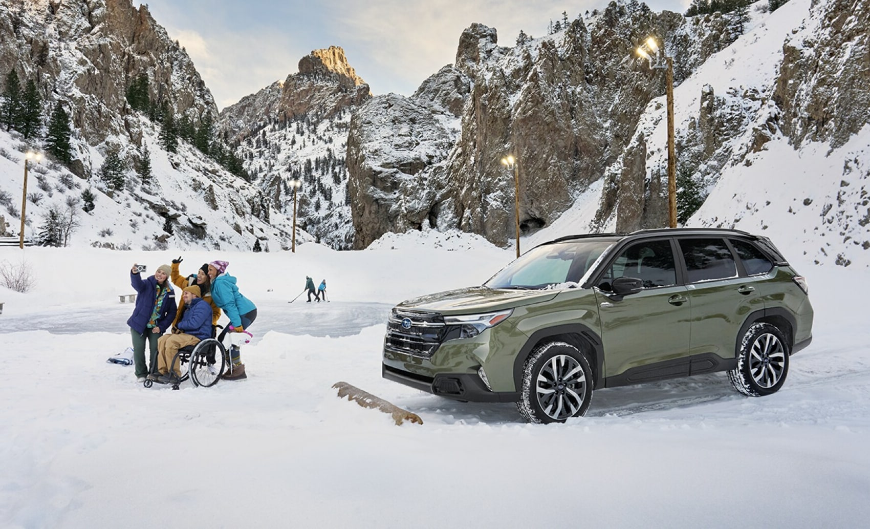  A Subaru Forester Hybrid parked on a snowy mountain road near a group of people gathered around a wheelchair user, with snow-covered cliffs and pine trees in the background under a partly cloudy sky.