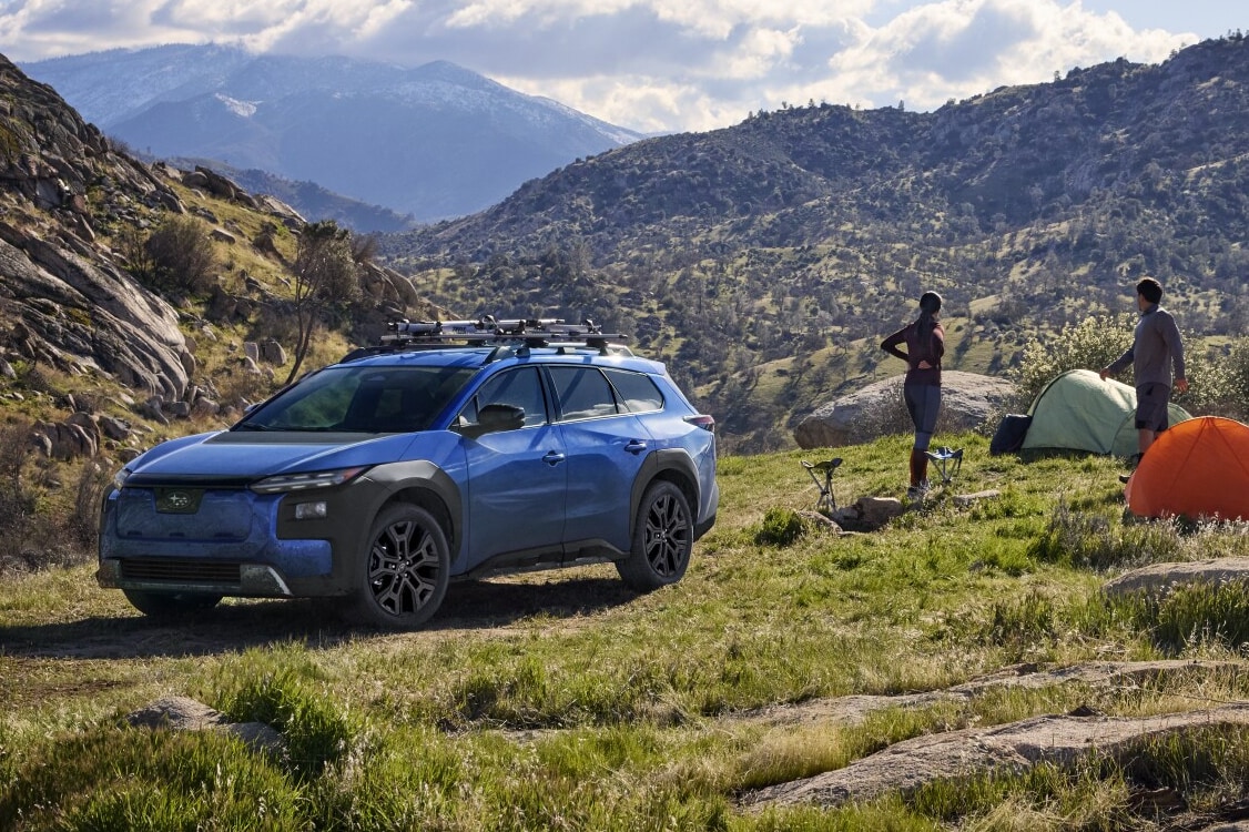  A static image of a blue 2026 Subaru Trailseeker parked on a grassy clearing in a rocky mountain landscape. 