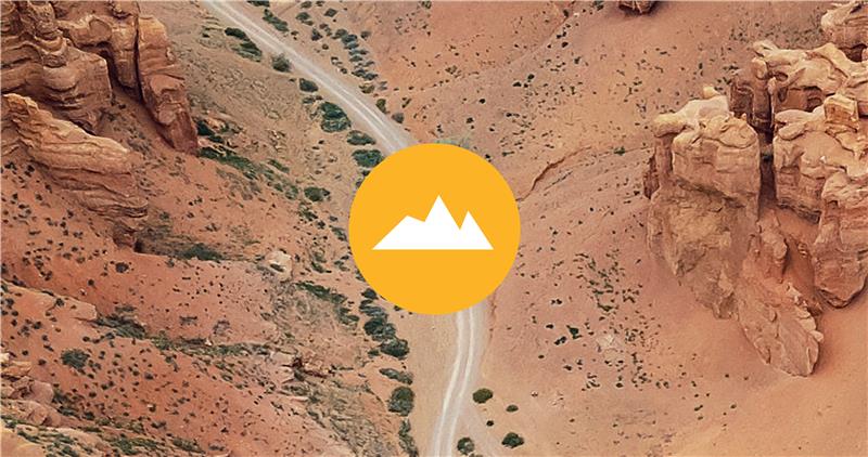 A white mountain icon on a yellow circle, overlaid on a rocky desert landscape.